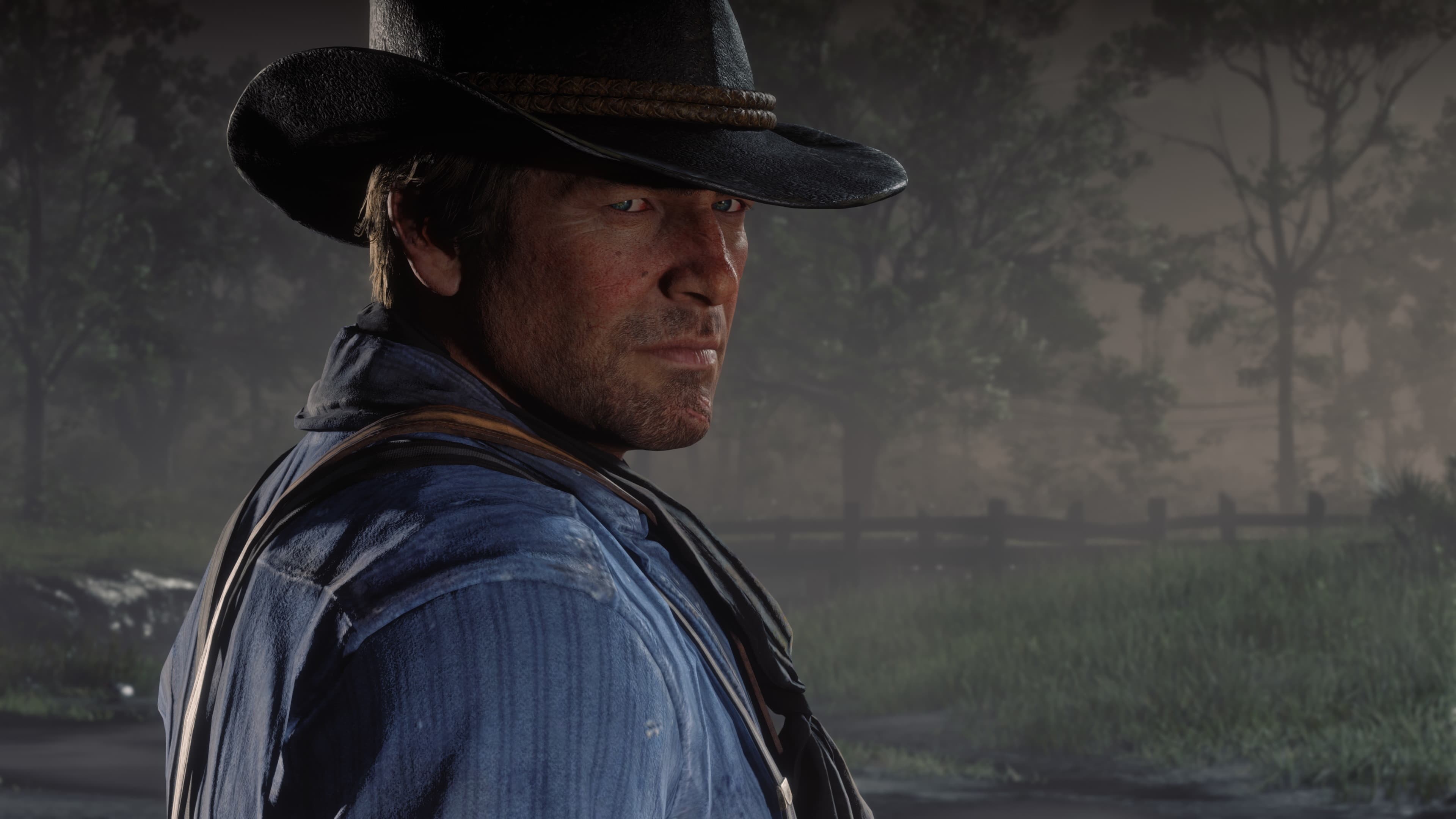A close view of a cowboy turning toward the camera, his face worn and serious, with misty woods behind him.